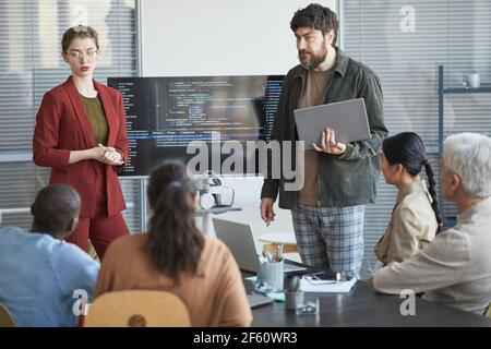 Portrait of mature bearded man giving presentation in office to diverse IT team standing by code on screen Stock Photo
