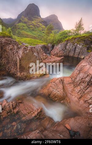 Idyllic mountain landscape along the River Coe to the Three Sisters of Glencoe with a colourful sunset or sunrise in the Scottish Highlands, Scotland. Stock Photo