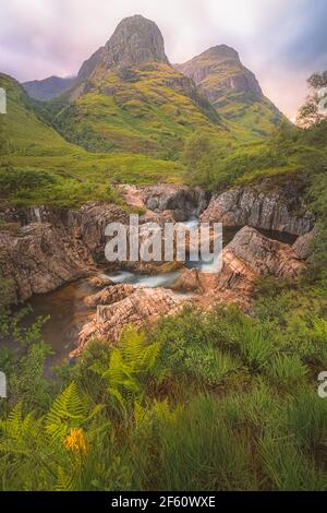 Idyllic mountain landscape along the River Coe to the Three Sisters of Glencoe with a colourful sunset or sunrise in the Scottish Highlands, Scotland. Stock Photo