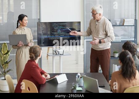 Portrait of modern senior man giving presentation in office to IT team and pointing at code on screen, copy space Stock Photo