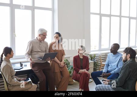 Wide angle view at contemporary diverse business team sitting in circle during strategy meeting, focus on senior businessman talking, copy space Stock Photo