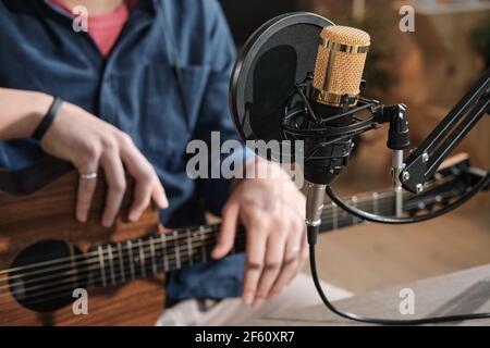 Close-up of man sitting in front of microphone and playing guitar in studio Stock Photo
