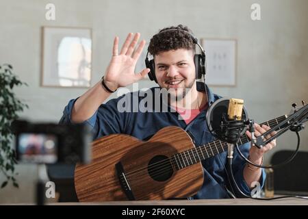 Portrait of mature man in headphones smiling at camera while waving his hands and playing guitar Stock Photo