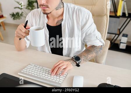 Cropped image of graphic designer with digital tablet drinking morning coffee and checking e-mails on computer Stock Photo