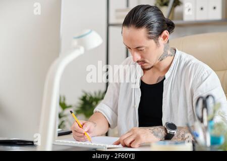 Serious concentrated creative graphic designer drawing sketch of logo with pencil on paper sheet Stock Photo