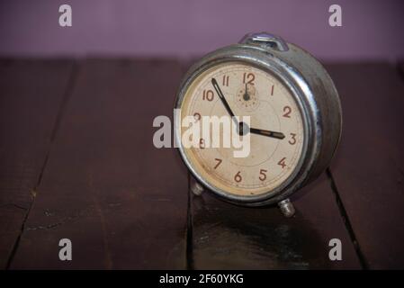 Old and retro alarm clock on wooden surface. Vintage background. Decor object. Time marker. Analog clock. Clock on dark background. Stock Photo