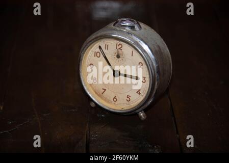 Old and retro alarm clock on wooden surface. Vintage background. Decor object. Time marker. Analog clock. Clock on dark background. Stock Photo