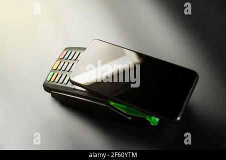 Using smartphone for contactless payment in a shoping, Electronic contacless terminal with cellphone on black background. Stock Photo