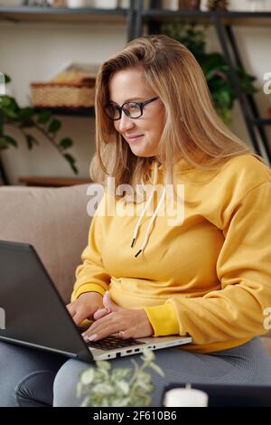 Pretty smiling young female softaware developer in glasse working on laptop at home Stock Photo