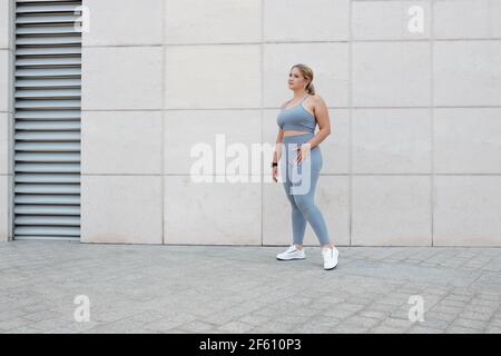 Full-length portrait of young fit plus size woman in grey sports bra and leggings standing outdoors Stock Photo