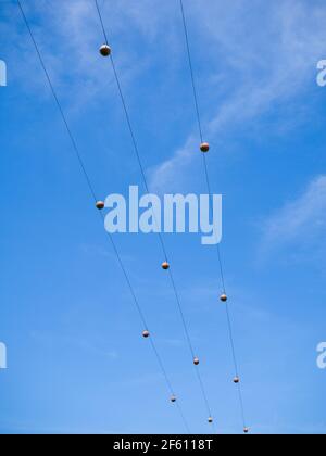 Aerial marker balls on three phase 11kv electricity power lines against a blue sky in the UK. Stock Photo