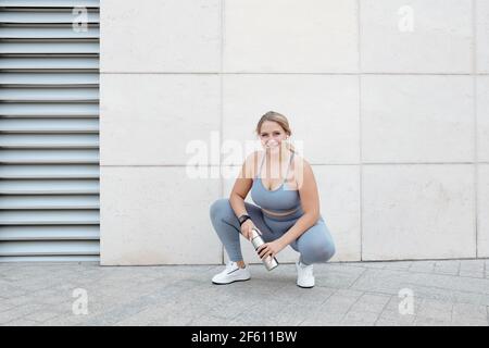 Happy pretty young fit plus size young woman resting after training and drinking water