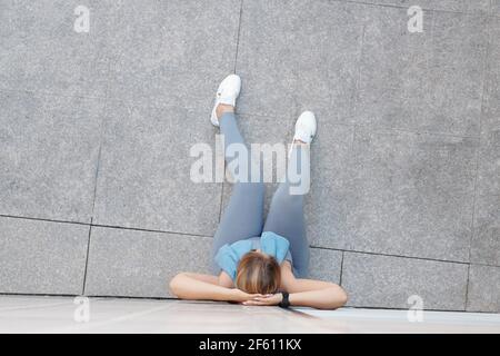 Plus size young woman resting on ground and leaning on wall when resting after intense outdoor training Stock Photo
