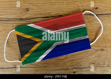 A surgical face mask with the painted flag of South Africa on a wooden background. Concept of South Africa during a pandemic, Covid-19, Coronavirus. Stock Photo