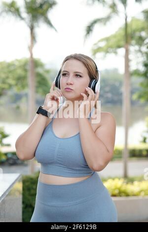 Pretty fit plus size young woman listening to music in headphones after traing outdoors