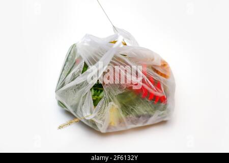 DEFOCUS. Save environmental. Red and green plants flowers in a plastic bag on a white background. A dry blade of grass sticks out. Ecological problems Stock Photo