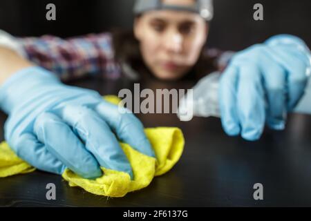 Female hands in rubber gloves with a rag spray detergent and wipe the table from dust and dirt. Housework. Cleaning of premises. 
