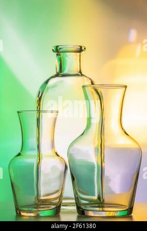 three items - transparent vases and a bottle. Still life abstract, on a colored yellow-green background. For design and decoration. Stock Photo