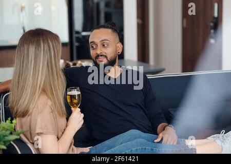 Smiling bearded man resting on sofa with girlfriend drinking champagne and telling about her day Stock Photo