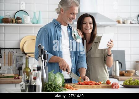 Beautiful couple using a digital tablet and smiling while cooking in kitchen at home. Stock Photo