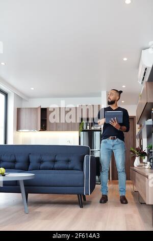 Handsome bearded man using application on tablet computer to control temperature and light in his studio apartment Stock Photo