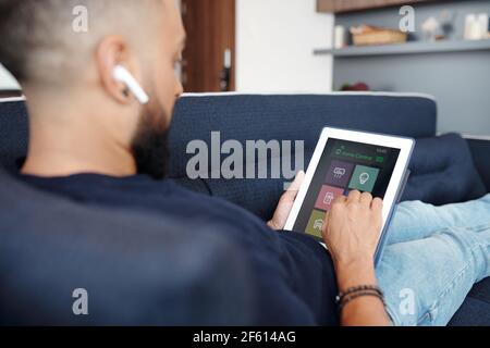 Close-up image of man using home control application on digital tablet when resting on sofa Stock Photo