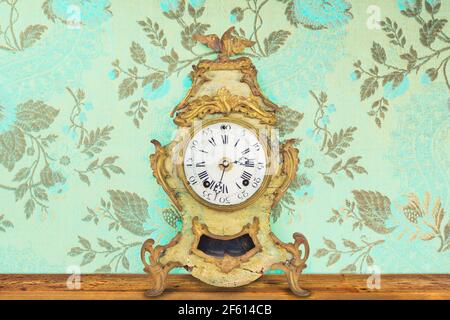 Interior with authentic eighteenth century weathered table clock in front of wallpaper with flower pattern Stock Photo