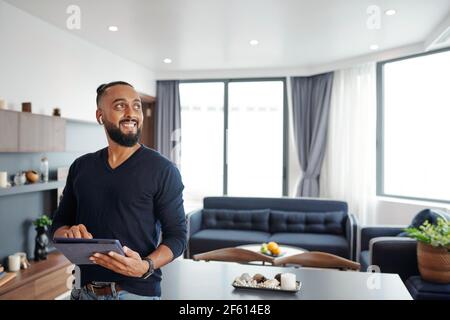 Portrait of happy excited bearded man using smart home application on digital tablet to open curtains and turn off light in his apartment Stock Photo