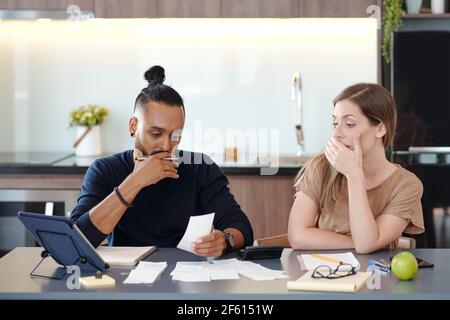 Young mixed-race couple covering mouth as they are shocked with sum in unpaid bill Stock Photo