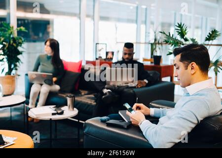 Male entrepreneur using smart phone while working with colleagues in office Stock Photo