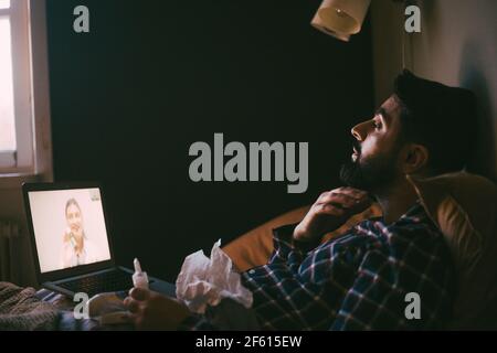 Man taking advice from doctor on video call through laptop at home during pandemic Stock Photo