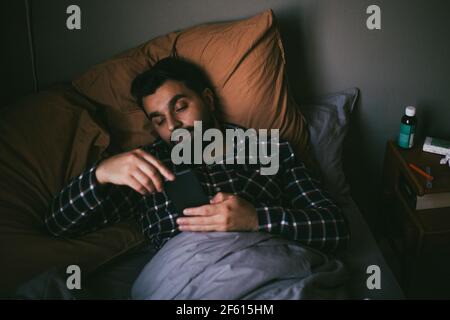 Sick man using smart phone while lying on bed at home Stock Photo