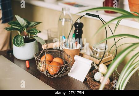 Easter day. Painted eggs in basket on wooden table at kitchen. Preparing for Easter, creative homemade decoration with plants Stock Photo
