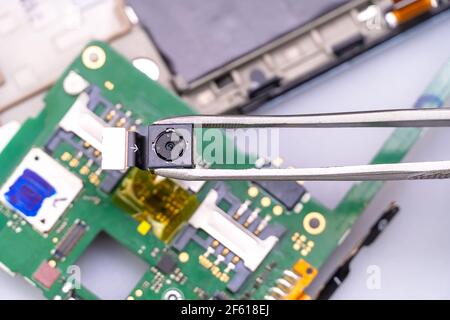 Fix the phone.A technician or master repairs a mobile phone, he installs and changes the camera in the motherboard. Hands, gloves, macro Stock Photo