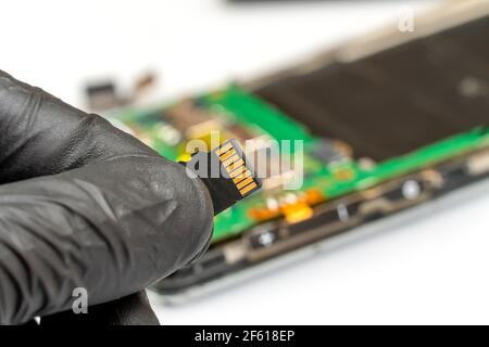 Technician worker holds a microSD card in a repair service center in front of a disassembled smartphone close up Stock Photo