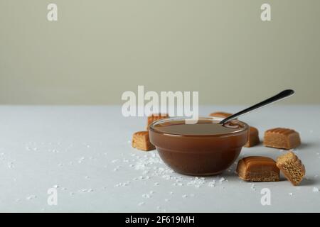 Salted caramel pieces and bowl of sauce on light gray table Stock Photo