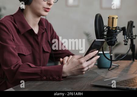 Close-up of radio reporter sitting at the table with laptop and using mobile phone at her work Stock Photo