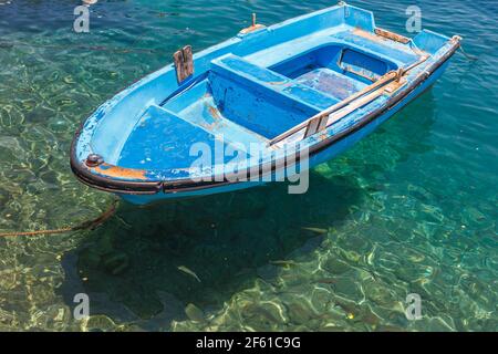 Old boat bobs on the crystal clear water surrounded by shoals of fish Stock Photo