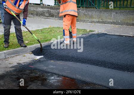 Paving workers adjust new layer of asphalt with shovels in reconstruction of road Stock Photo