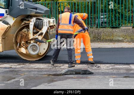 Paving workers add asphalt in front of wheel roller - road reconstruction