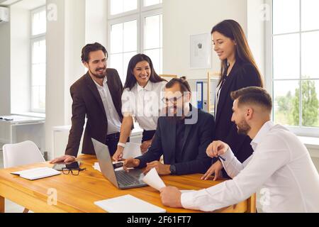 Happy company workers gather in office and use laptop computer for marketing research or video call Stock Photo