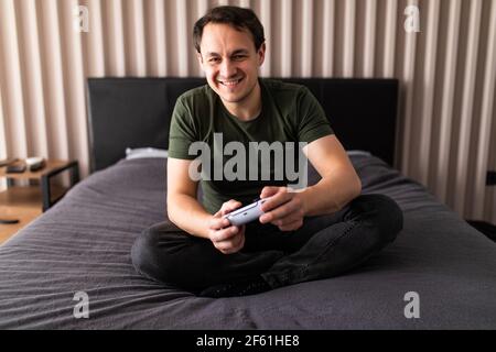 Attractive man holding joy stick and playing videogames on tv at vacation, sits at home on the cozy couch Stock Photo