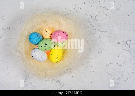 Multicolored Easter eggs in a nest on a white concrete background. View from above. Stock Photo
