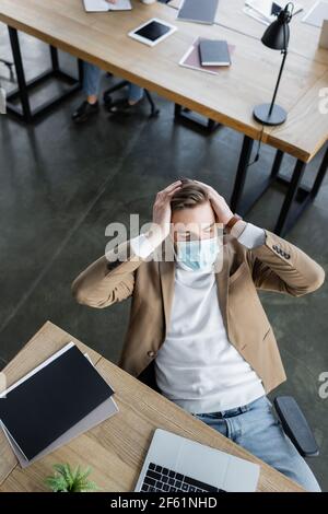 high angle view of tired businessman in medical mask suffering from headache in office Stock Photo