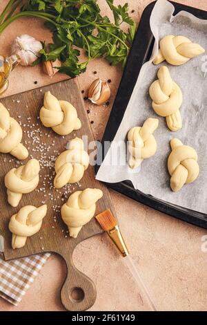 Baking sheet and board with uncooked garlic buns on color background Stock Photo