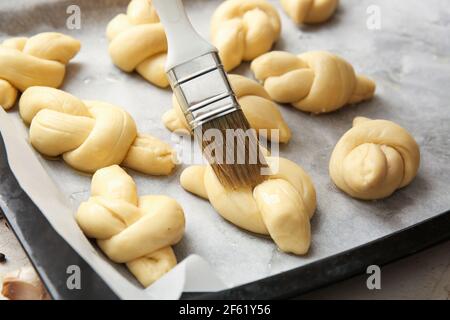 Greasing uncooked garlic buns with oil on baking sheet, closeup Stock Photo