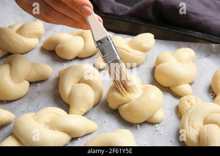 Woman greasing uncooked garlic buns with oil on baking sheet Stock Photo