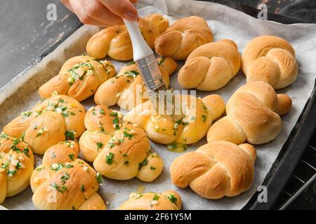 Woman greasing tasty garlic buns with oil on baking sheet, closeup Stock Photo