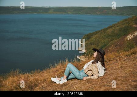 Young female hiker relaxing on mountain peak and enjoying beautiful nature at Bakota bay. Happy woman in cowboy hat spending leisure time at national ukrainian park. Stock Photo