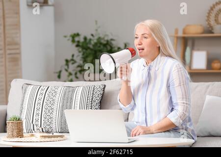 Screaming mature woman with megaphone at home Stock Photo